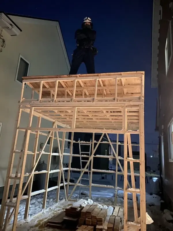 札幌の便利屋サービス創業者が自身で建てた小屋の上で腕を組み笑顔で立つ姿(創業の原点)