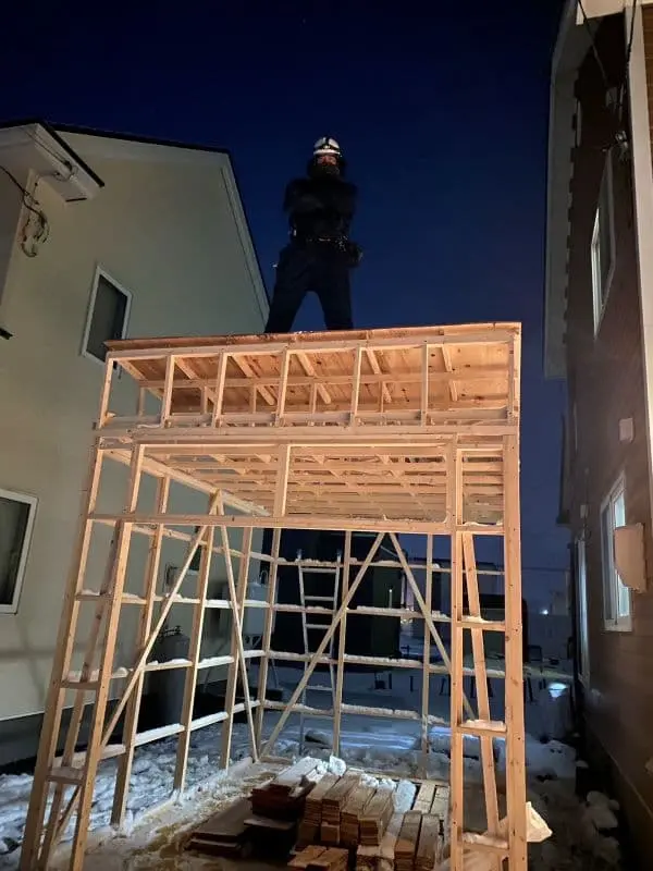 札幌の便利屋サービス創業者が自身で建てた小屋の上で腕を組み笑顔で立つ姿